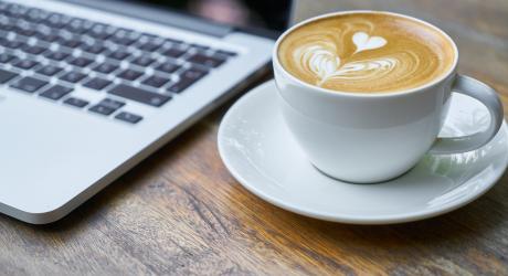 A coffee on a wooden table next to a laptop