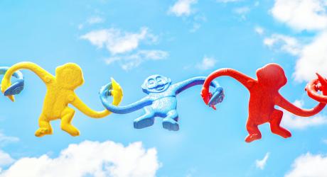 Three toy monkeys holding hands against a cloudy background