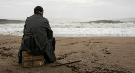 Man staring out at the ocean from the beach, sitting on wooden boxes
