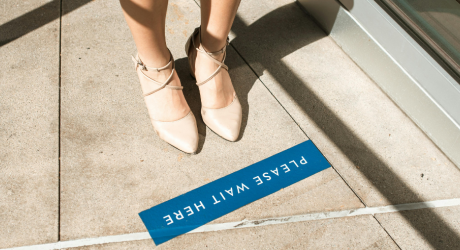 A lady standing behind a sign saying "Please wait here"