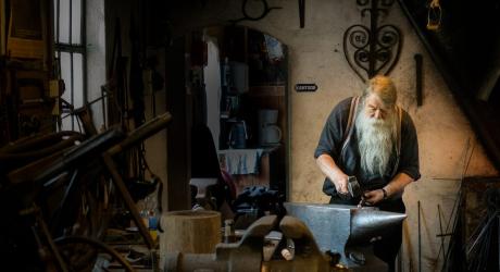 An old man in a workshop carefully crafting a piece of metal with a hammer and an anvil.