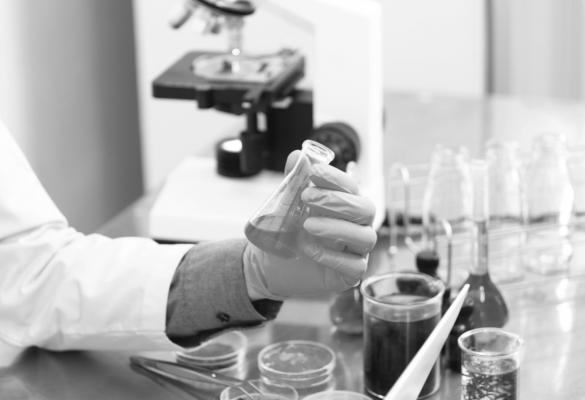 A close up of gloved hands in a lab holding a small beaker