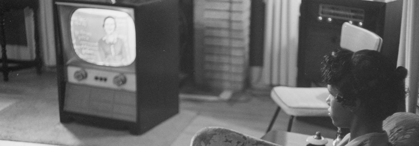An atmospheric angle peering over the shoulder of a young girl watching the tv set, it's the 1950s so it's a tiny tv in a big box.