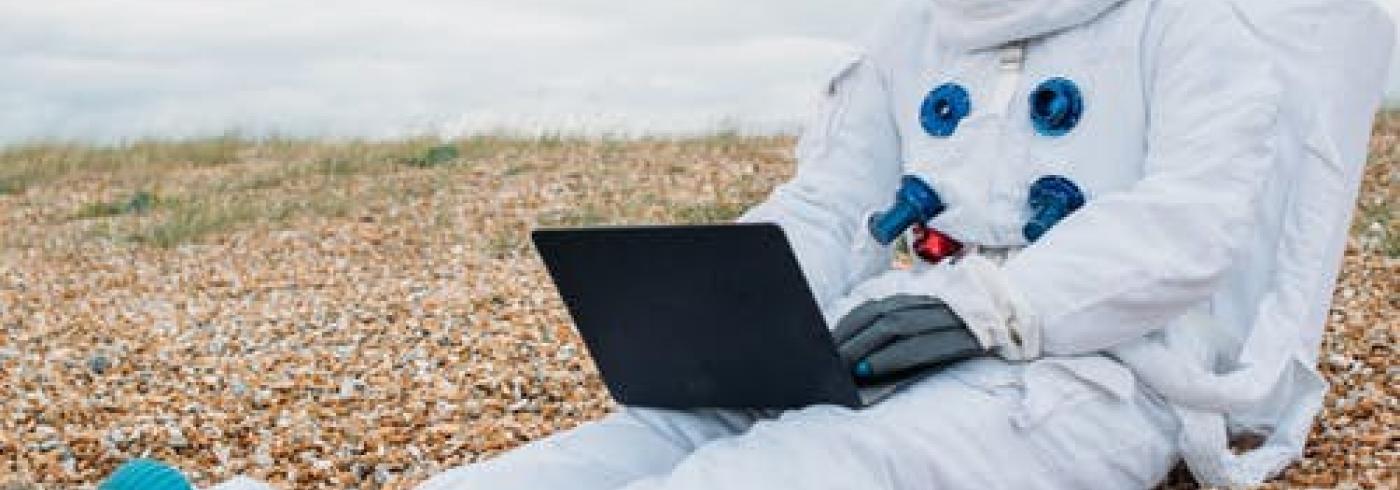 An astronaut sitting on a beach with a laptop