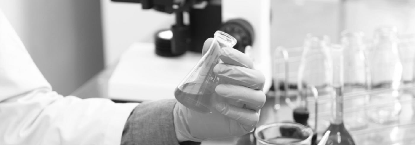 A close up of gloved hands in a lab holding a small beaker