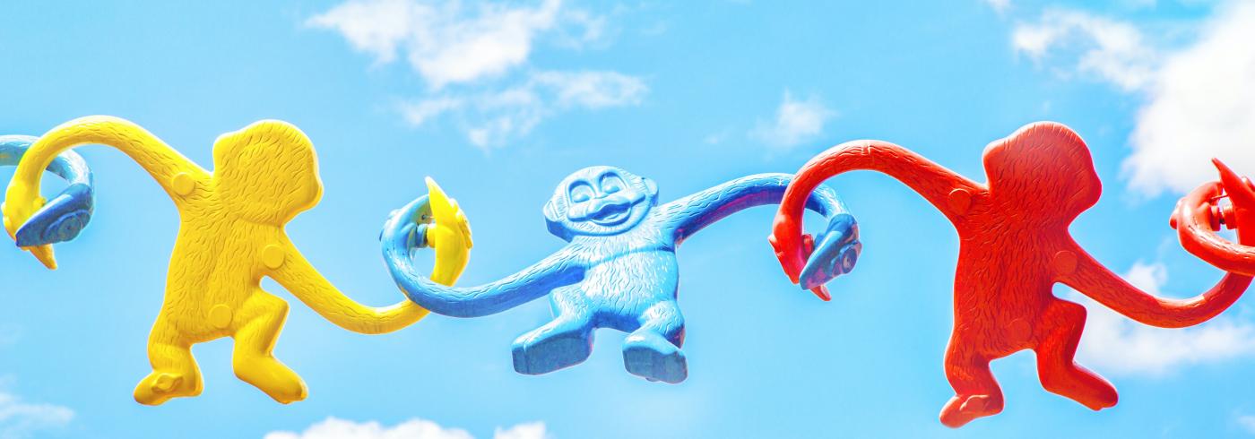 Three toy monkeys holding hands against a cloudy background