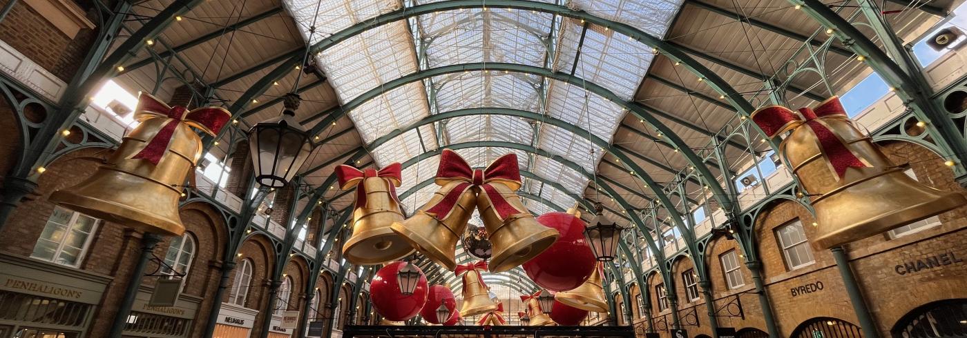 A view of Covent Garden at Christmas time with large golden bell and red ribbon decorations hanging from the rafters.