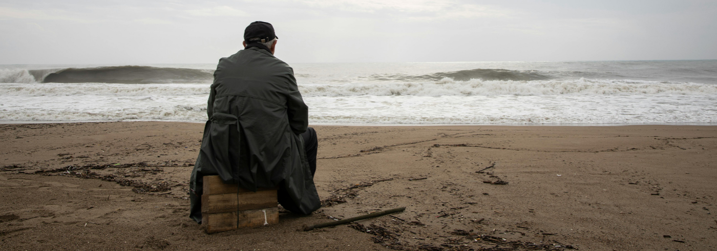 Man staring out at the ocean from the beach, sitting on wooden boxes