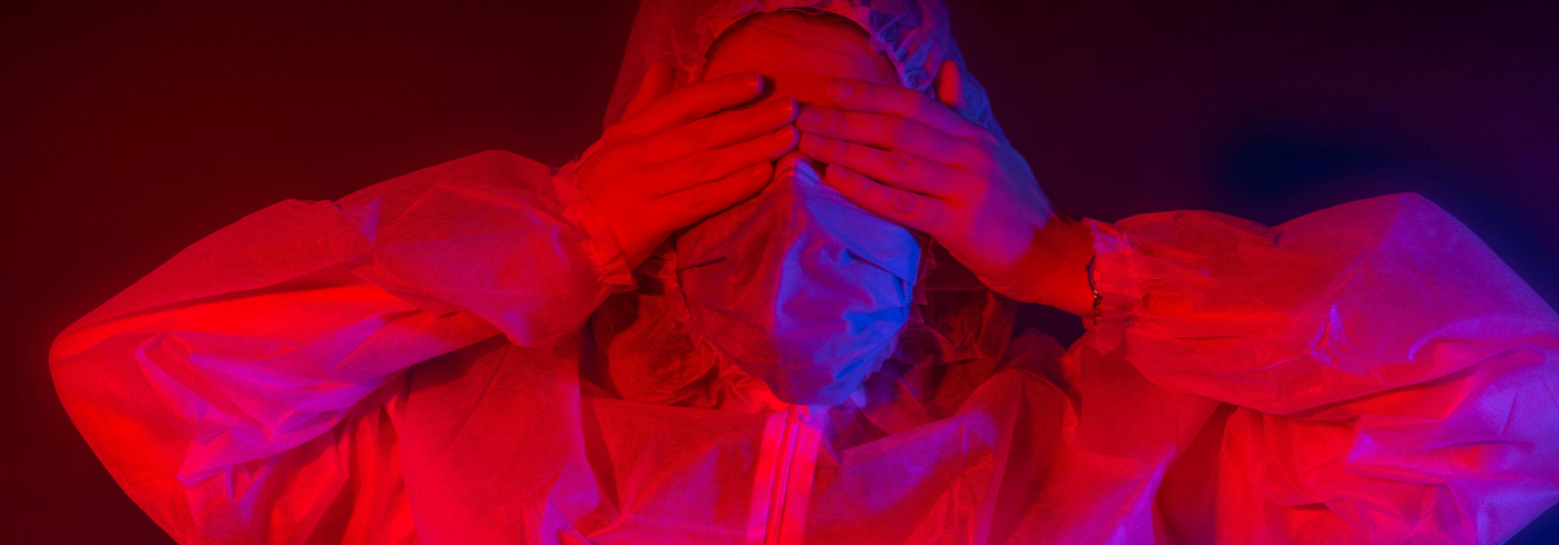 A person in PPE hiding their eyes behind their hands