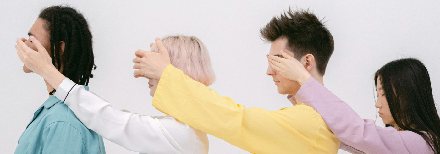 4 people in a line, each covering the eyes of the person in front